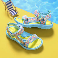 Sandale Fille avec Damier Multicolore sur les Lanières posée au bord d'une piscine à côté d'un mini transat sur fond jaune