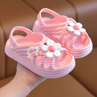 Sandale Fille Rose Conception Mignonne avec Fleur, dans une main, sur un fond marron.