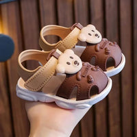 Sandale Meduse Bebe au Design d'Ourson dans la main d'une personne sur fond marron