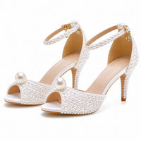 Sandale femme mariage à talon avec des perles blanche. La chaussure présente un talon fin très haut blanc d'environ 8-10 cm avec finition caramel-doré contrastante, une semelle plateforme épaisse blanche avec finition caramel-doré, une couverture complète très généreuse de perles blanches nacrées qui ornent l'ensemble du dessus du pied créant un effet très luxueux et spectaculaire, deux grandes perles blanches nacrées suspendues élégamment sur la semelle avant, une bride de cheville réglable densément ornée
