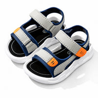 Sandales ouvertes pour garçon bleu marine et grises avec scratchs réglables, détails orange et semelle blanche confortable.