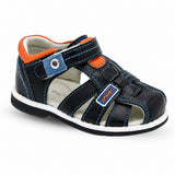 Sandale garçon plate en simili-cuir noir. La chaussure présente une semelle plate blanche contrastante, un corps en simili-cuir noir avec accents orange et détails bleu ciel, une fermeture velcro/scratch réglable avec panneau denim bleu ciel et œillet métallique, découpes ajourées latérales pour l'aération, doublure intérieure grise très confortable, coutures décoratives bleu ciel tout autour, badge "SPORT" broché, design très sportif et ludique adapté aux enfants. Présentée sur fond blanc.