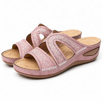 Sandale orthopédique femme compensée style vintage rose poudré. La chaussure présente une semelle épaisse compensée en taupe beige, une bride croisée rose poudré ornée de broderies blanches avec motifs floraux et détails géométriques, des découpes ajourées en forme de cœur sur le dessus pour plus d'aération, une semelle intérieure confortable aérée. Design inspiré des années 1970, présenté sur fond blanc.
