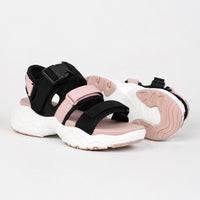 Sandale sport femme à scratch et semelle épaisse. La chaussure présente une semelle plateforme très épaisse blanc et rose contrastant avec profil profilé épais, des bandes de maintien en tissu noir et rose poudré, une fermeture velcro/scratch noire réglable sur le cou-de-pied, doublure intérieure rose, design très sportif et volumineux. Présentée sur fond blanc.