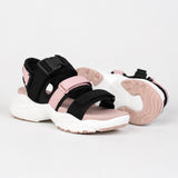 Sandale sport femme à scratch et semelle épaisse. La chaussure présente une semelle plateforme très épaisse blanc et rose contrastant avec profil profilé épais, des bandes de maintien en tissu noir et rose poudré, une fermeture velcro/scratch noire réglable sur le cou-de-pied, doublure intérieure rose, design très sportif et volumineux. Présentée sur fond blanc.