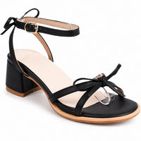 Sandale talon femme 5 cm noire avec nœud de papillon. La chaussure présente un talon carré noir de 5 cm de hauteur, une semelle plate avec finition contrastante beige-taupe, des lanières croisées minimalistes en noir, deux nœuds de papillon noirs très élégants - un sur le pied et un à la cheville, une bride de cheville réglable avec boucle dorée, doublure intérieure beige. Design très féminin et sophistiqué. Présentée sur fond blanc.