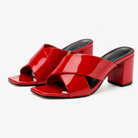 Sandale talon femme 5 cm rouge et luxueuse en cuir. La chaussure présente un talon carré rouge laqué brillant, des lanières croisées en cuir rouge vernis à finition très brillante, semelle plate carrée rouge, doublure noire contrastante, design très moderne et luxueux. Présentée sur fond blanc.