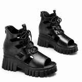 Sandale talon plateforme semi-ouverte avec lacets noire. La chaussure présente une semelle plateforme ultra-épaisse en caoutchouc noir texturé avec motifs de rainures profilées très volumineux, un talon compensé très épais noir assorti, un design semi-ouvert avec découpes ajourées latérales, des lacets noirs pour l'ajustement, plusieurs bandes noires de maintien, une fermeture arrière réglable, doublure intérieure noire, design très moderne avant-garde et tendance. Présentées sur fond blanc.