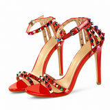Sandale Cloutée Style Escarpin avec Lanière de Cheville rouge avec brides ornées de clous pyramidaux multicolores, boucle réglable à la cheville, bout ouvert et talon aiguille pour un style chic et élégant.