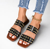 Sandale Femme Cloutée avec Deux Lanières noires, à doubles brides ornées de clous pyramidaux dorés, bout carré, semelle plate confortable et design tendance