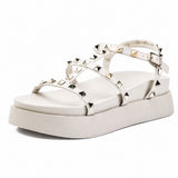 Sandale Talon Plateforme avec Lanières Cloutées Blanches avec fines brides ornées de clous pyramidaux métalliques, boucle réglable à la cheville, bout ouvert et semelle plateforme épaisse pour un style moderne et tendance.