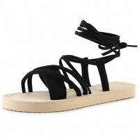 Sandale à lanière femme confortable et épaisse noire. La chaussure présente une semelle plateforme plate très épaisse en crème-beige avec profil texturé épais, plusieurs lanières croisées en suède noir qui s'entrecroisent sur le pied, une bride arrière noire réglable avec lacet de serrage, design très minimaliste et confortable. Présentée sur fond blanc.