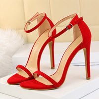 Sandale à talon femme effet daim et élégante rouge. La chaussure présente un talon très haut et fin rouge avec finition beige-taupe contrastante, un bout ouvert, une bride de cheville réglable avec boucle métallique carrée, des lanières minimalistes en daim rouge velouté, semelle plate avec doublure beige. Design très sophistiqué et luxueux. Présentée sur fond blanc avec accessoires féminins.