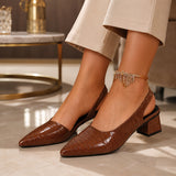 Sandales escarpins à talon carré marron crocodile. La chaussure présente un talon carré marron-chocolat d'environ 5-6 cm de hauteur, un corps en cuir embossé motif crocodile/alligator très brillant marron foncé, un bout fermé pointu très élancé, une bride arrière ouverte très sophistiquée, doublure intérieure marron contrastante, semelle plate marron, design très élégant fusion escarpin-sandale. Portée avec une robe beige-crème fluide et bracelet chaîne dorée ornée de strass, dans un intérieur haut de gamme