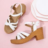 Sandales habillées confortables beige-blanc. Les chaussures présentent une semelle taupe texturée, des lanières tressées blanches croisées sur le dessus du pied, une bride de cheville blanche réglable avec boucle dorée, un design très élégant et confortable. La paire du bas présente un talon carré en bois texturé avec semelle plateforme épaisse en bois tressé. Présentées sur fond rose pastel.