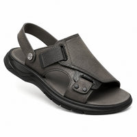 Sandales en cuir confortables avec maintien renforcé gris-noir. La chaussure présente une semelle plate très épaisse en caoutchouc noir texturé antidérapant avec profil ergonomique épais, un corps en cuir gris-noir souple très confortable, une bride arrière réglable avec anse de maintien supérieure en cuir gris, une fermeture velcro/scratch noire avec détail de logo métallisé, plusieurs bandes de maintien latérales avec rivets noirs, doublure intérieure gris-noir très confortable et aérée, design très fonct