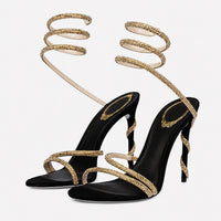 Sandales À Talon Femme Avec Brides Spirales Chic noires avec fines brides dorées scintillantes, lanières spirales autour de la cheville, bout ouvert et talon aiguille pour un style élégant et raffiné.