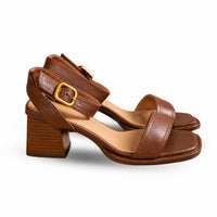 Sandales à talons confortables en cuir marron clair. Les chaussures présentent un talon carré bloc en bois marron clair texturé, une semelle plate en cuir marron, des lanières minimalistes en cuir marron uni, une bride de cheville réglable avec boucle carrée dorée, doublure intérieure beige contrastante, design très élégant et confortable. Présentées sur fond blanc.