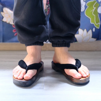 Sandale Japonaise Style Tong avec Semelle en Bois portée par un homme avec un pantalon noir et des motifs floraux en fond