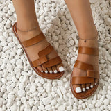 Sandale Plate Femme avec Lanières Épaisses et Design portée par une femme sur des cailloux blanc